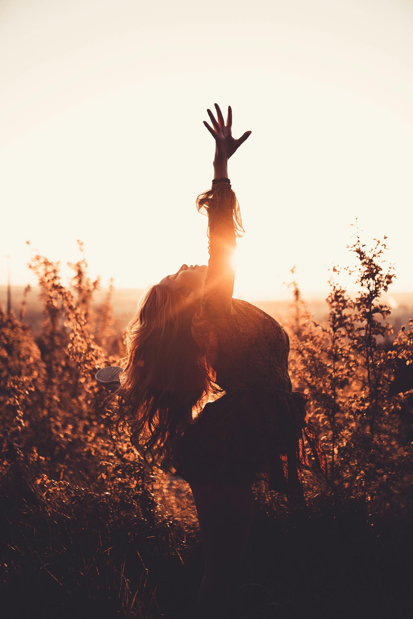 Side view of graceful woman leaning back with raised leg while dancing between shrubs in countryside in back lit